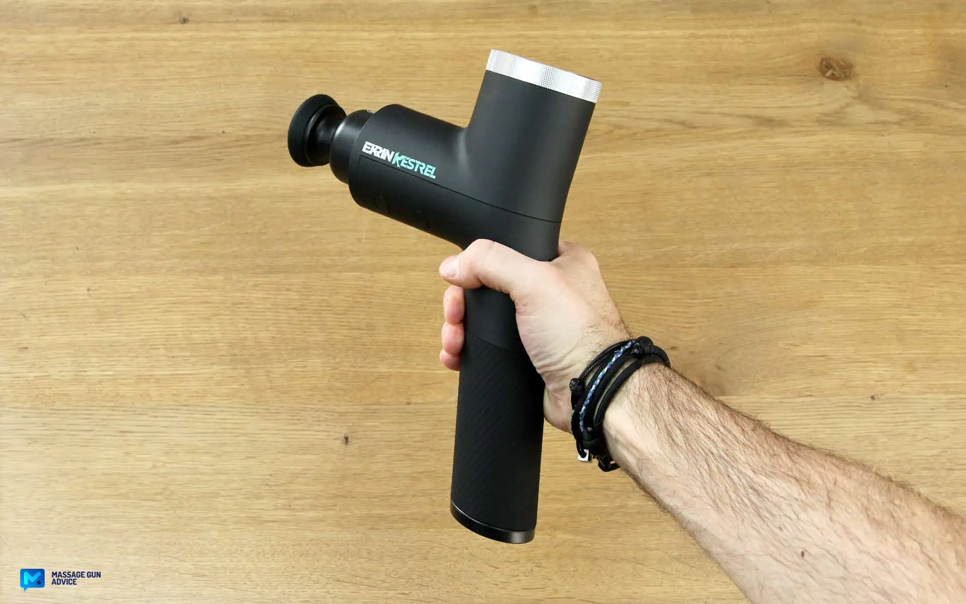 Ekrin Kestrel Review - Is This the Ultimate Massage Gun Unicorn? 18 most powerful massage gun: Ekrin Kestrel held by its 15 degree angle handle. A Hand holds it on a wood-like background.