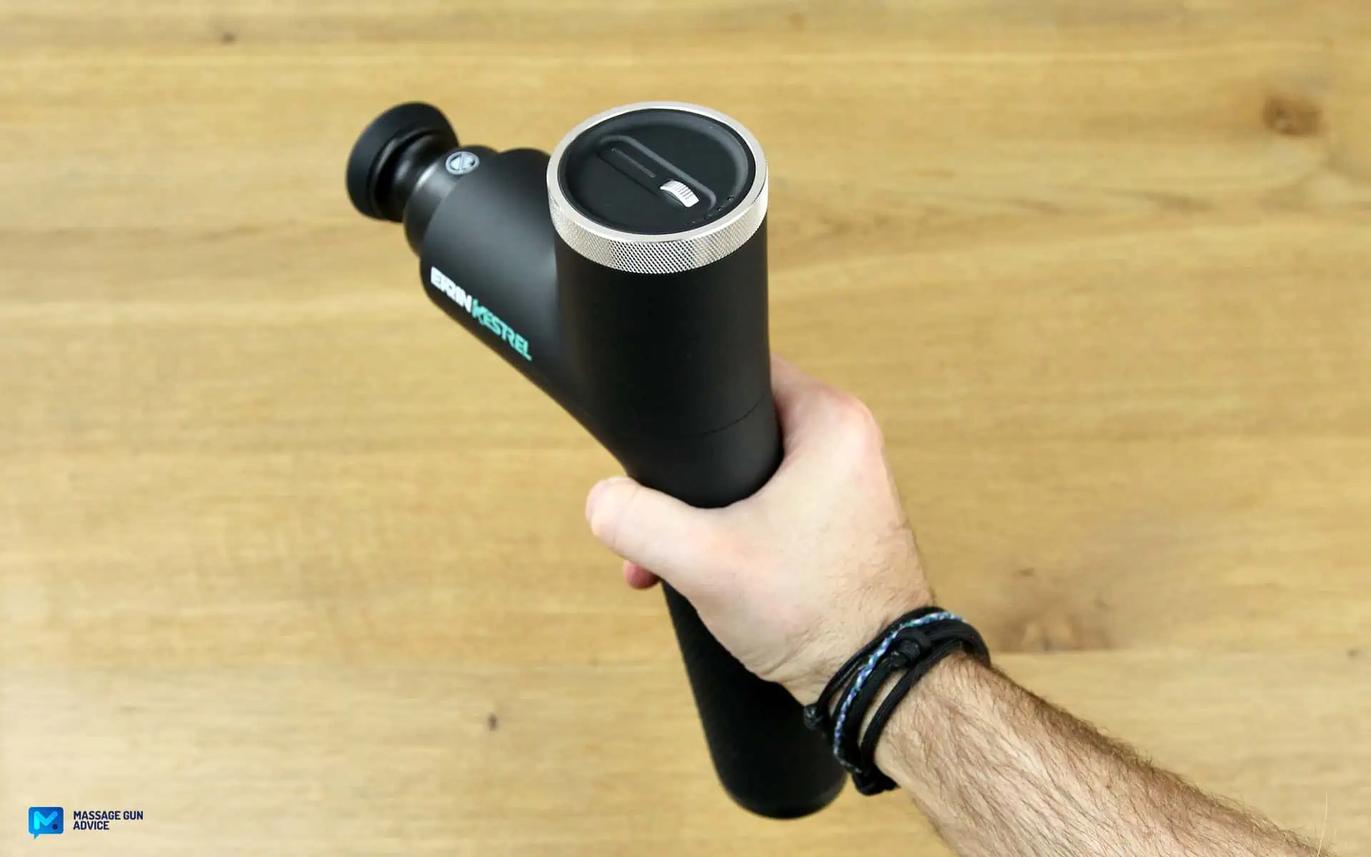 Ekrin Kestrel Review - Is This the Ultimate Massage Gun Unicorn? 17 strongest massage gun: top-side view of the Ekrin Kestrel held by Hand on a wood-like background